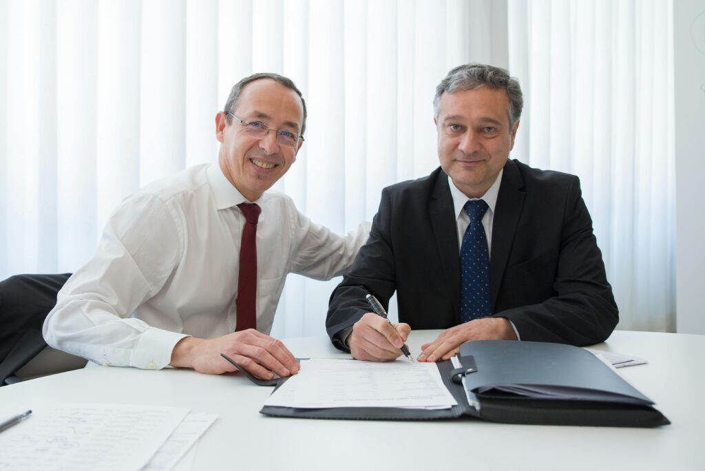 pexels-photo-8428073-8428073 Two businessmen in suits signing a contract at a well-lit office table.